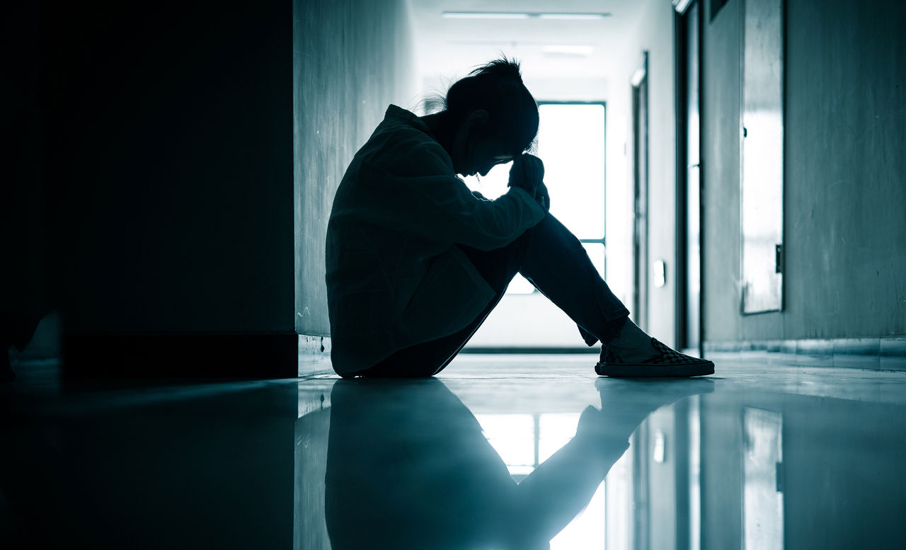 upset teen sitting in a hallway with head down