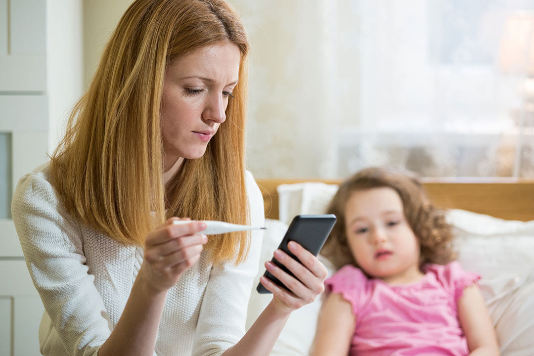 Mom with sick child scheduling an appointment with phone